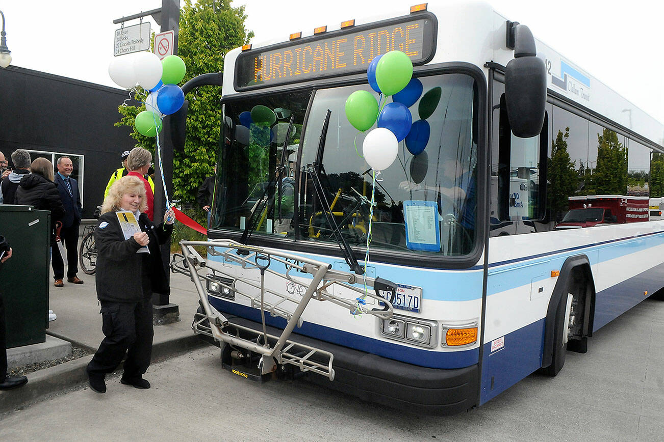 Clallam Transit operations supervisor Rickie Stimbert attaches balloons to the front of the first bus to make scheduled service from The Gateway transit center to Hurricane Ridge on Wednesday. (Keith Thorpe/Peninsula Daily News)