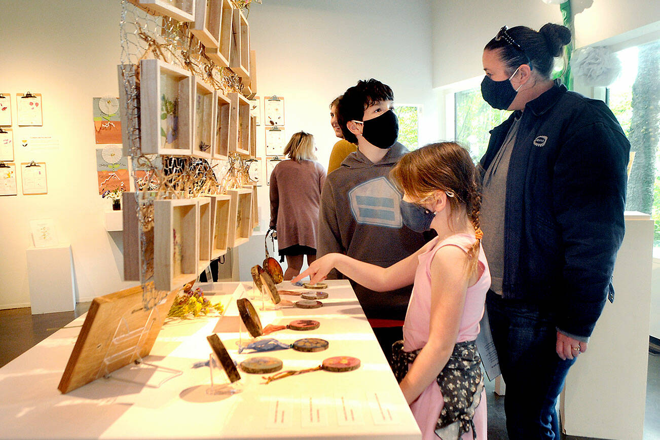 Alice Cordery, 7, a first-grade student at Jefferson Elementary School in Port Angeles, front, points to an artwork as her brother, Pat Cordery, 11, and mother, Teresa Cordery, follow along during an opening gala for Blooming Artists, an exhibition of nature-related art pieces on Tuesday at the Port Angeles Fine Arts Center. (Keith Thorpe/Peninsula Daily News)