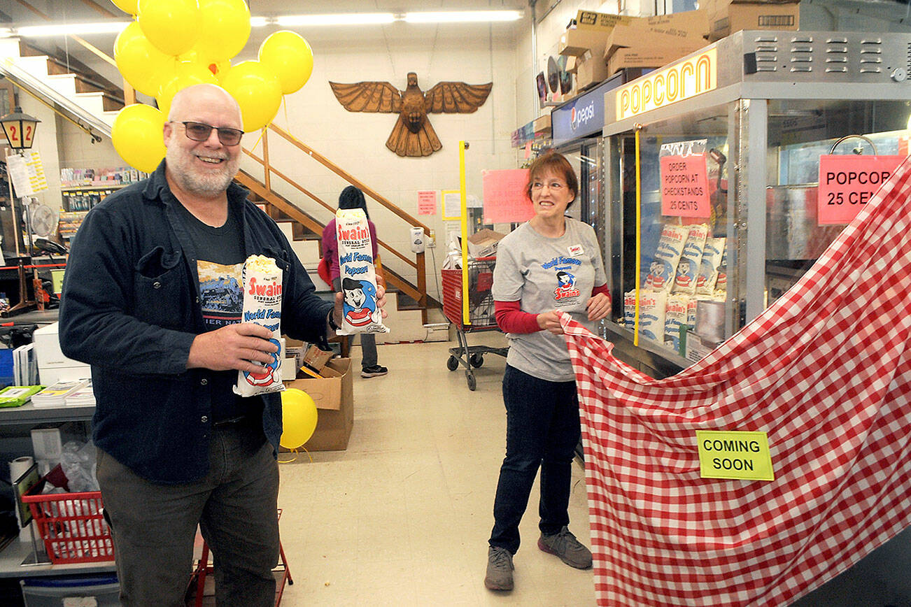 Ernie Latson of Port Angeles, left, purchases the first two bags of popcorn as Swain’s General Store employee Shawn Price unveils the popcorn machine on Wednesday morning in Port Angeles. The store, which is celebrating its 65th anniversary this year, resumed selling its signature popcorn after a two-year hiatus imposed by COVID-19 health measures. The price remains the same as it was when Swain’s first offered it to customer in 1966 — 25 cents. (Keith Thorpe/Peninsula Daily News)