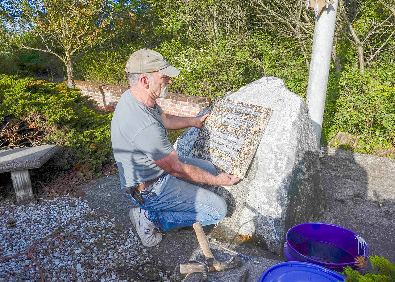 Robert Parker, a self-employed contractor from Port Orchard, installs a granite plaque honoring Navy Seabee Marvin G. Shields, who died in June 1965 in Vietnam and was awarded the Medal of Honor for heroism, at the Marvin Shields Memorial Flagpole on a stone monument from which the original bronze plaque was stolen in 2019. “He is very precious to us,” said Parker, an ex-Navy Seabee who volunteered to place the plaque. “This plaque is granite so there is less incentive for thieves,” he added. The Admiralty Inlet Chapter of the Daughters of the American Revolution will dedicate the memorial plaque at 1 p.m. Saturday in the small park on the north side of West Sims Way between Sheridan and Tenth streets. (Steve Mullensky/for Peninsula Daily News)