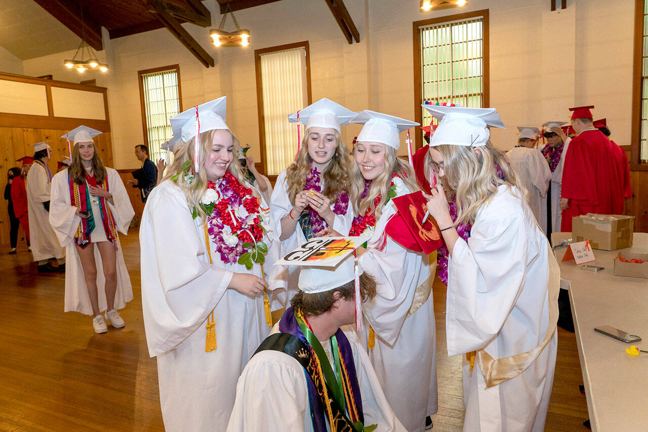 Port Townsend High School’s Sidda Hayes, Macy Smith, Charlotte Falge and Maddi Witheridge look over Tusker Behrenfeld’s mortar board to decipher the meaning. Eighty-two seniors received their diplomas before family and friends during the 132nd Commencement at McCurdy Pavilion on Friday night. (Steve Mullensky/for Peninsula Daily News)