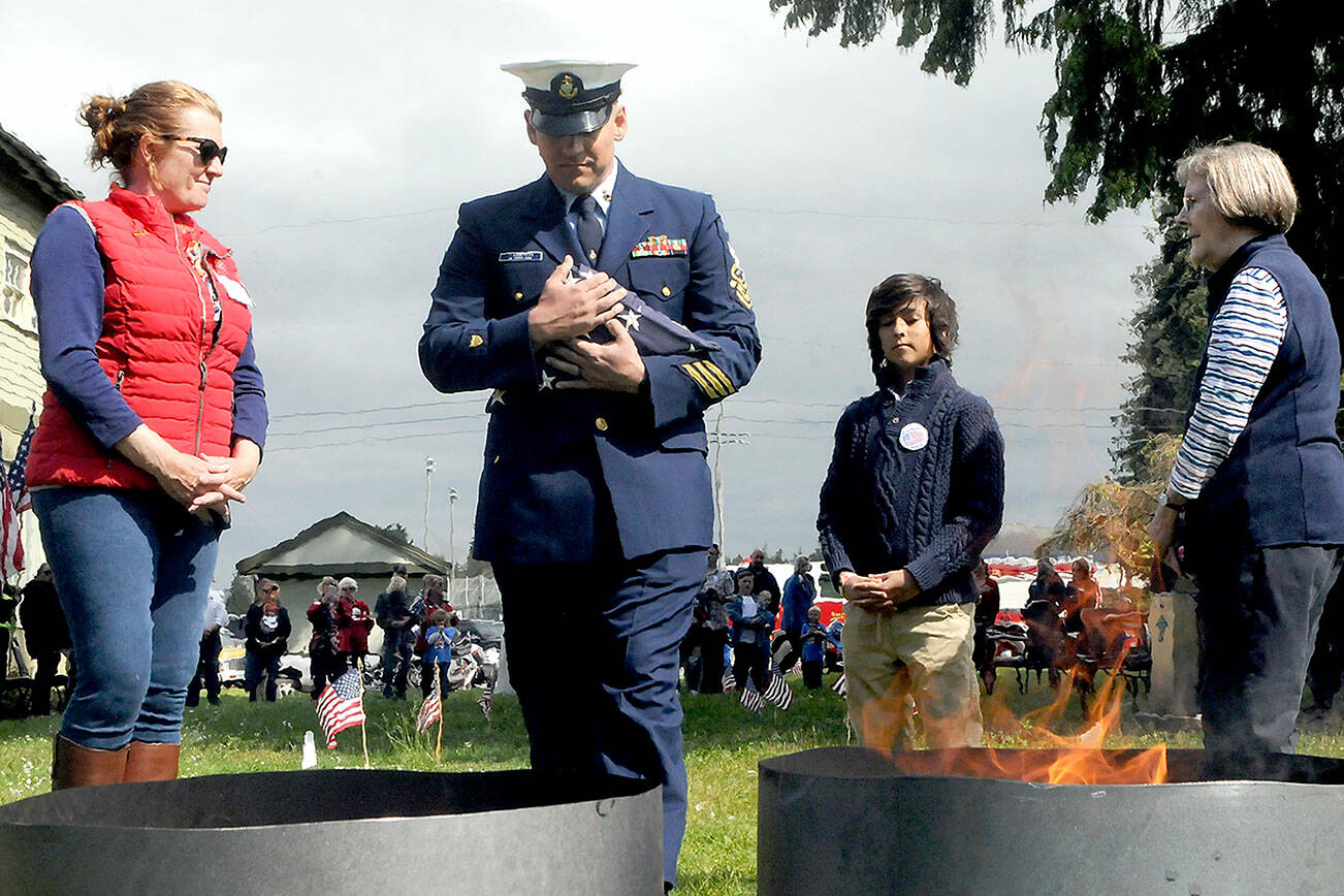Keith Thorpe/Peninsula Daily News
U.S. Coast Guard Chief Petty Officer Shane Thompson, accompanied by his son, Malachi Thompson, 10, a member Junior American Citizens, carries a used flag for inceneration on Tuesday at the Northwest Veterans Service Center in Port Angeles on Flag Day. Overseeing the burning were Ginny Sturgeon, left, and Jan Urfer, right, members of the Michael Trebert chapter of the Daughters of the American Revolution, which co-hosted the event with the Clallam County Veterans Association. Eleven used cotton flags were burned during Tuesday's Flag Retirement Ceremony.