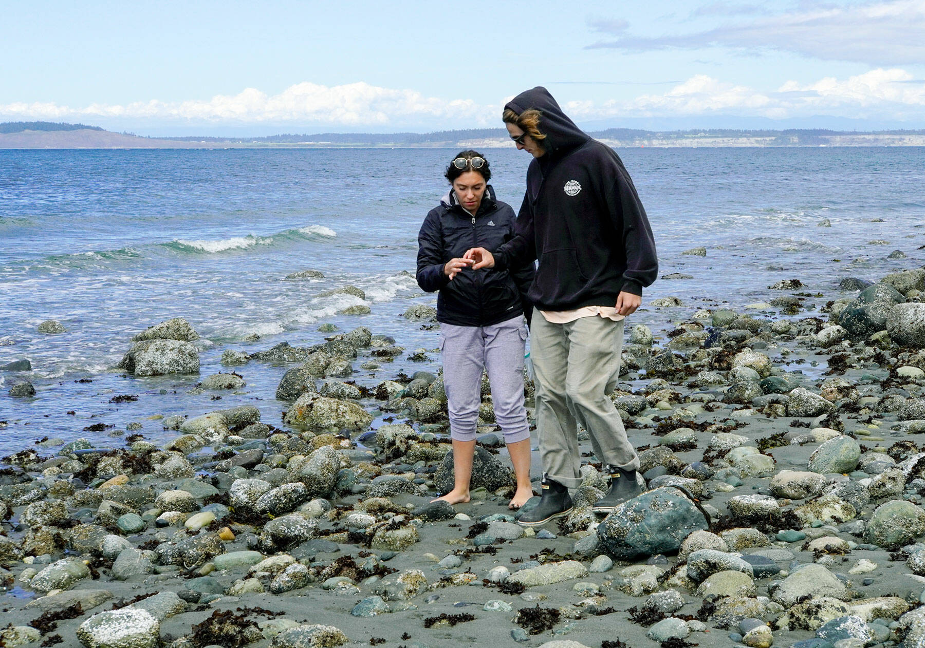 Maren Gillette and Austin Tyree, on a road trip from Wenatchee, examine a piece of beach glass they picked up on the beach at North Beach in Port Townsend on Wednesday. (Steve Mullensky/for Peninsula Daily News)