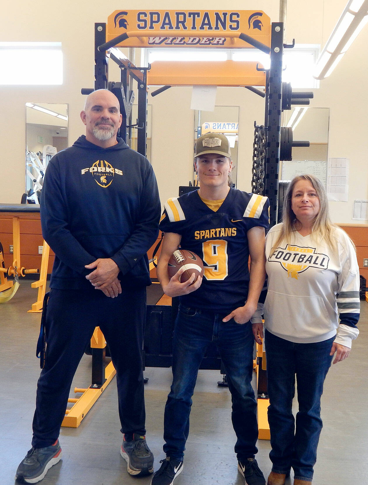 Forks’ Dalton Kilmer, center, is one of five North Olympic Peninsula athletes who will play for the West team in the Class 2A/1A/B Earl Barden Classic, the all-state football game in Yakima on Saturday. Kilmer is joined by Forks football coach Trevor Highfield and his mom, Amy Kilmer. (Christi Baron/Olympic Peninsula News Group)