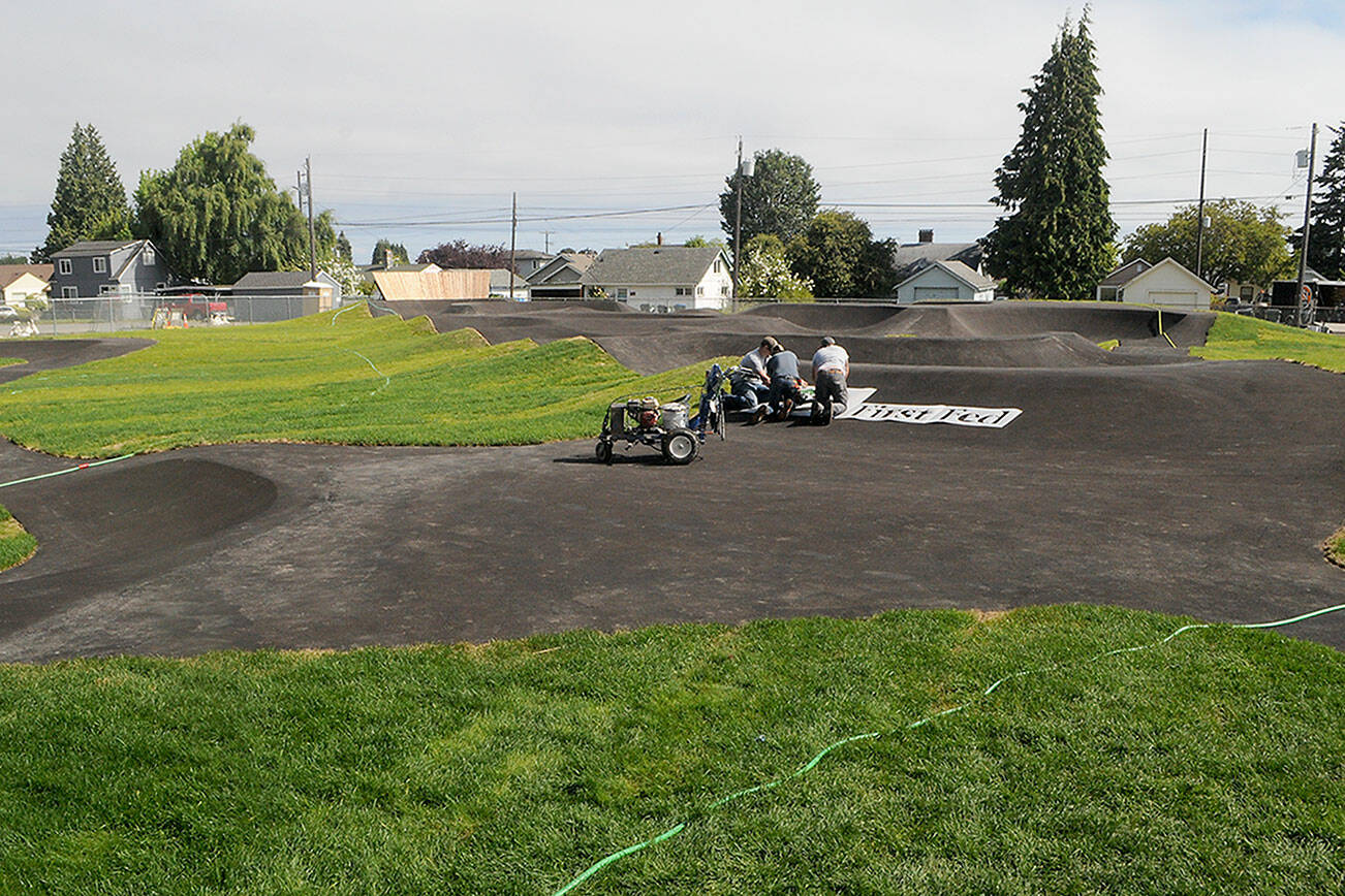 Keith Thorpe/Peninsula Daily News
A crew applies a sponsorship logo on the riding surface of a new pump track at Erickson Playfied in Port Angeles on Friday in preparation for the grand opening on Wednesday.