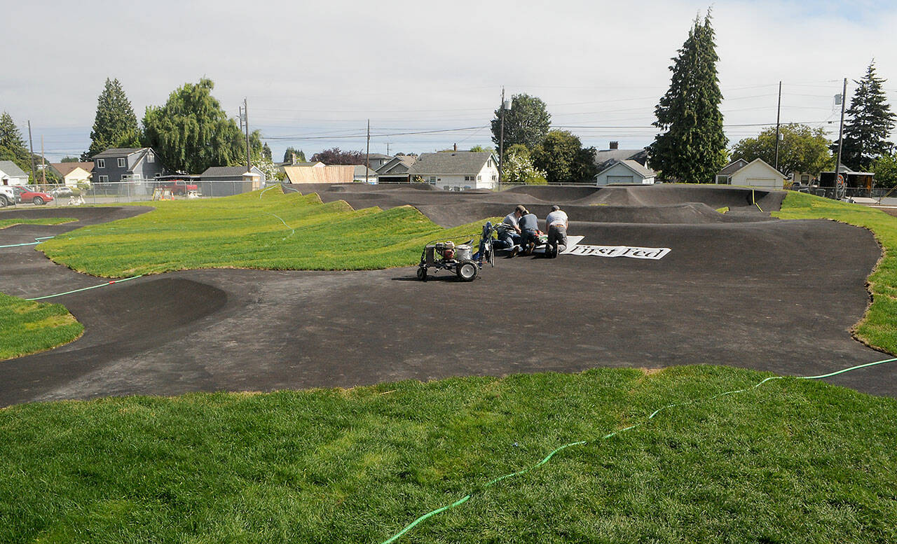 A crew applies a sponsorship logo on the riding surface of a new pump track at Erickson Playfied in Port Angeles on Friday in preparation for the grand opening on Wednesday. (Keith Thorpe/Peninsula Daily News)