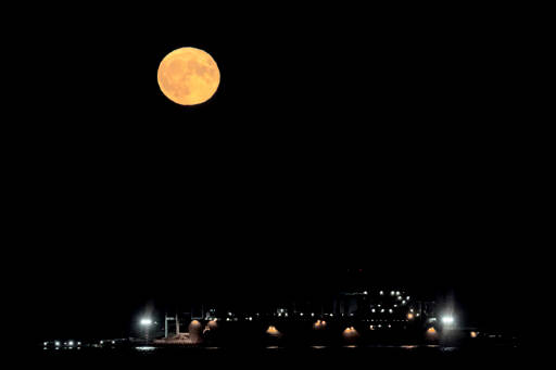 The full supermoon rises over the USNS Richard E Byrd moored at Naval Magazine Indian Island in Port Townsend Bay on Wednesday night. This is the last supermoon of the year. (Steve Mullensky/for Peninsula Daily News)