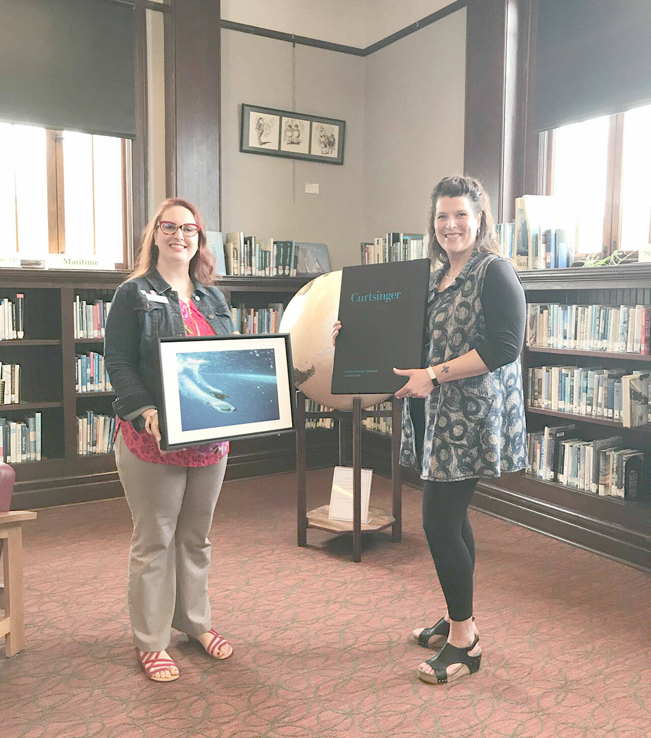 Melody Sky Weaver, on left, accepts a donated Bill Curtsinger photograph from Teresa Verraes, executive director of Northwind Art.
