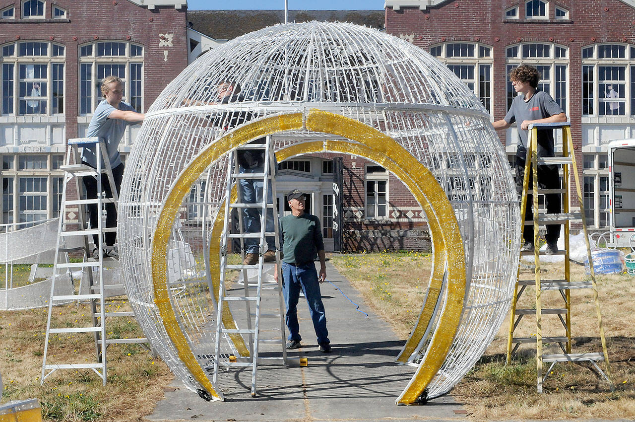 Rick Smith of the Olympic Medical Center Foundation, center, watches as Aidan Butterworth, left, Dave Jungck of Kent-based AV Factory, on ladder in middle, and Tanner McLean do a test assembly of a giant Christmas decoration on Wednesday on the front lawn of the old Lincoln School in Port Angeles. The decoration, donated by the Microsoft Corporation, will become part of a display in the foundations Festival of Trees in November, and then be incorporated into the Port Angeles Winter Ice Village in December. (Keith Thorpe/Peninsula Daily News)