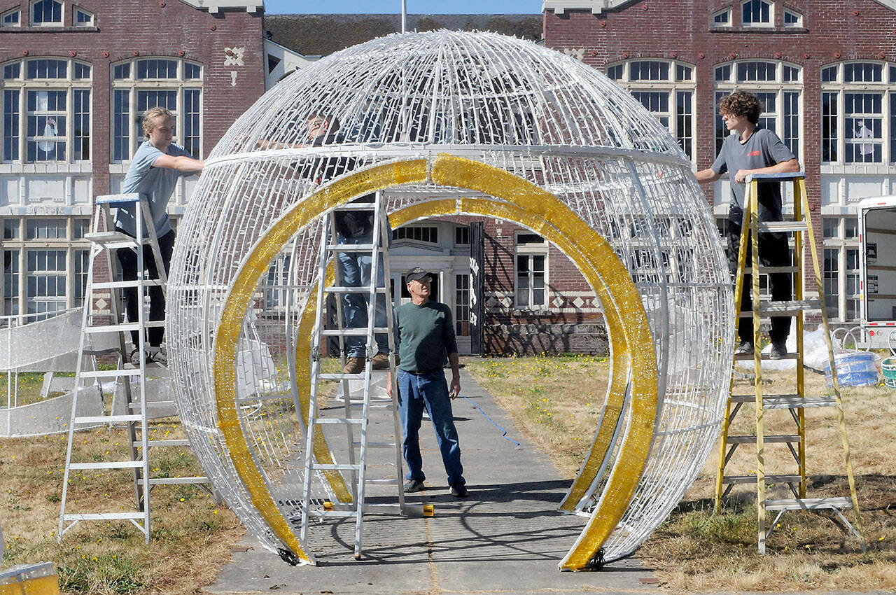 Rick Smith of the Olympic Medical Center Foundation, center, watches as Aidan Butterworth, left, Dave Jungck of Kent-based AV Factory, on ladder in middle, and Tanner McLean do a test assembly of a giant Christmas decoration on Wednesday on the front lawn of the old Lincoln School in Port Angeles. The decoration, donated by the Microsoft Corporation, will become part of a display in the foundation’s Festival of Trees in November, and then be incorporated into the Port Angeles Winter Ice Village in December. (Keith Thorpe/Peninsula Daily News)