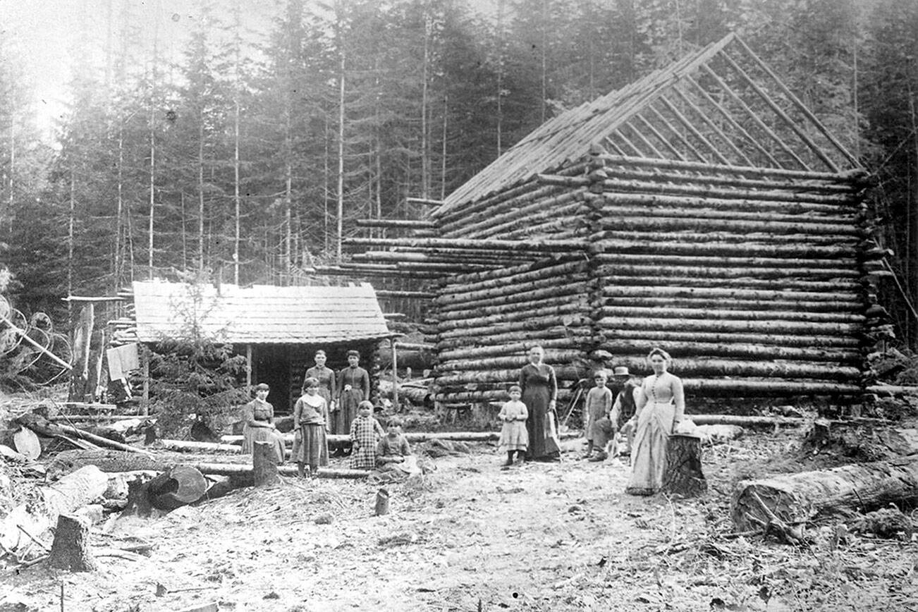 North Olympic History Center
A two story log cabin being built.  One man, four women and five children (Unidentified) are shown.  A smaller log cabin is beside the cabin under construction.