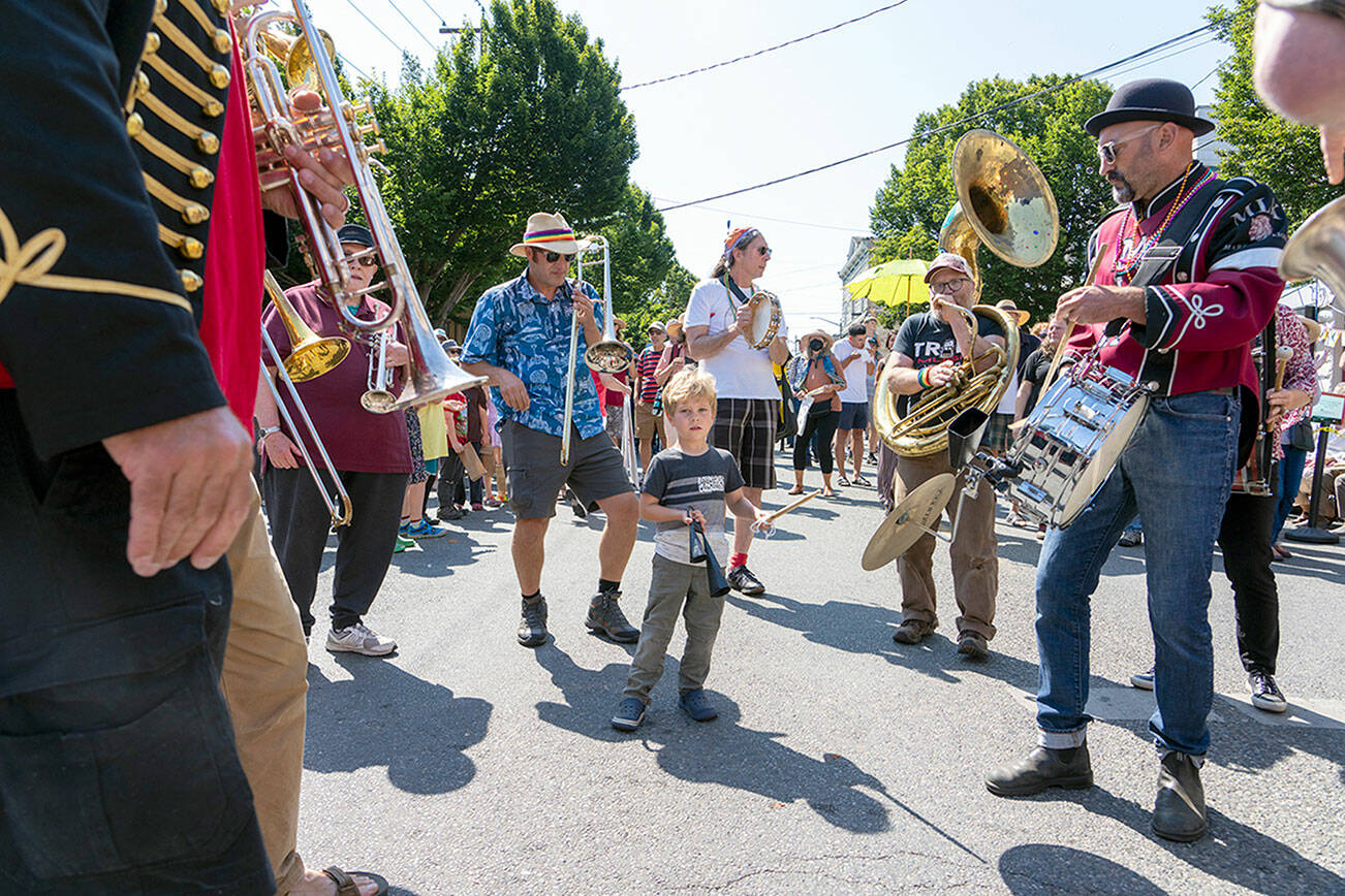 Rigel Orr, 5, center, playing a percussion instrument, might be the youngest member of the Unexpected Brass Band as they play during the Uptown Street Fair on Saturday. Dad Matt, in blue shirt, keeps a watchful eye on his son. (Steve Mullensky/for Peninsula Daily News)