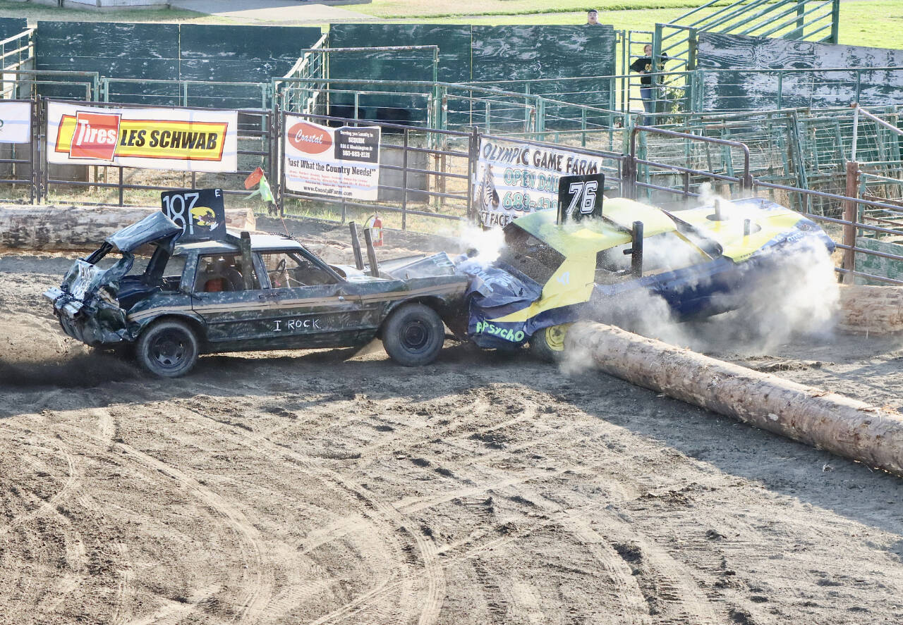 Demolition derby driver Morgan Seamonds (107) pushes Brandon Vale’s car (76) up and over a log barrier in a cloud of dust and exhaust in front of a sold-out crowd at the Clallam County Fairgrounds on Sunday evening. (Dave Logan/for Peninsula Daily News)