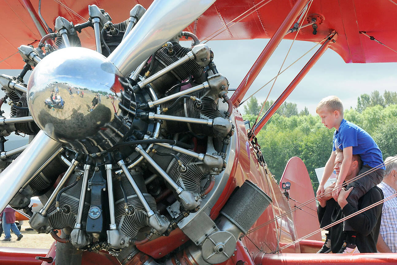 Grayson Kelm, 9, sits on the shoulders of his father, Jon Kelm of Happy Valley, Ore., to get a better look inside the cockpit of a Boeing Stearman PT-17 biplane at Air Affaire on Saturday at Sequim Valley Airport near Carlsborg. The event featured an aircraft fly-in, along with displays, airplane and helicopter rides, a car show, food and live music. (Keith Thorpe/Peninsula Daily News)