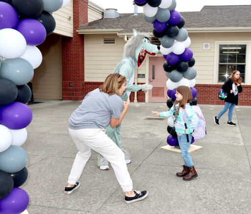 Alliannah Soehgen, a first-grader, is greeted by the Jefferson Elementary School mascot, the wolf, and the school’s principal, Rhonda Kromm, as they go through a balloon arch and enter the school for the first day on Thursday. (Dave Logan/for Peninsula Daily News)