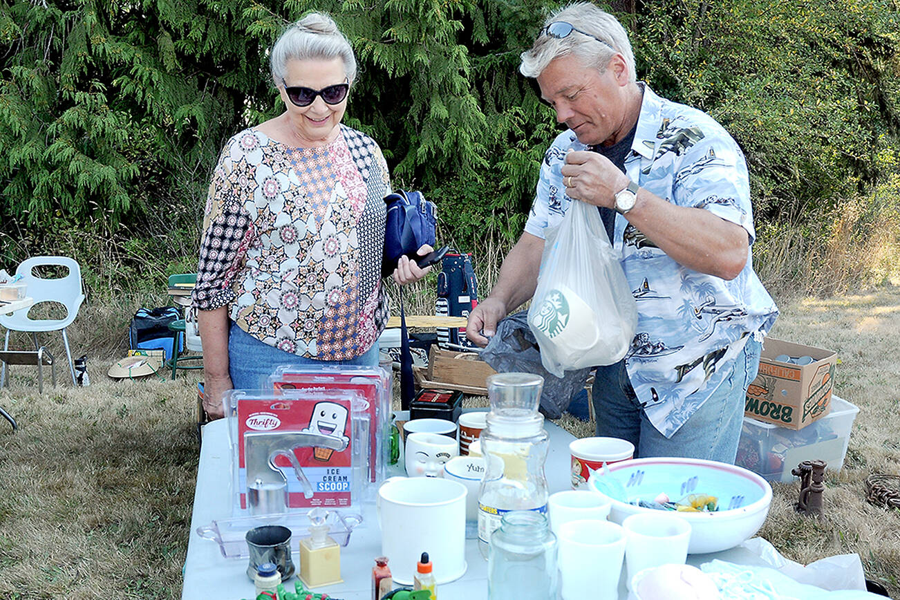 KEITH THORPE/PENINSULA DAILY NEWS
Marlene McCurdy of Port Angeles, left, purchases coffee mugs from Gary Gort of Port Angeles at a sale table in front of the Crescent Grange Hall in Joyce on Saturday. The location was one of dozens of garage and yard sales taking part in the Great Strait Sale, stretching along and near State Highway 112 from Port Angeles to Neah Bay.