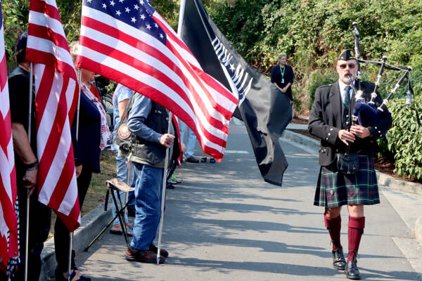 Rick McKenzie starts Sunday’s ceremony at the 9/11 Memorial Park with bagpipe music, walking down the line of flags to the memorial of a 9-foot I-beam from the Twin Towers in New York. About 2,000 of these memorial pieces of wreckage have been placed around the country. (Dave Logan/for Peninsula Daily News)