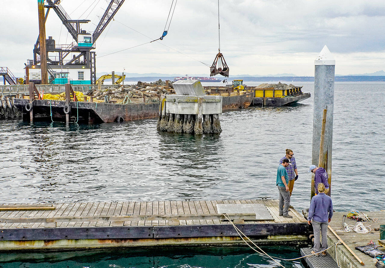 A crew from the Northwest Maritime Center facilities department, Sam Trocano, Jeff Hogue, Shane Meyer and Mike Conklin, work on the removal of the floating dock on the center’s pier in preparation of winter winds and weather. In the background, work continues on the deconstruction of the entrance to the Point Hudson Marina by Orion of Tacoma. (Steve Mullensky/for Peninsula Daily News)