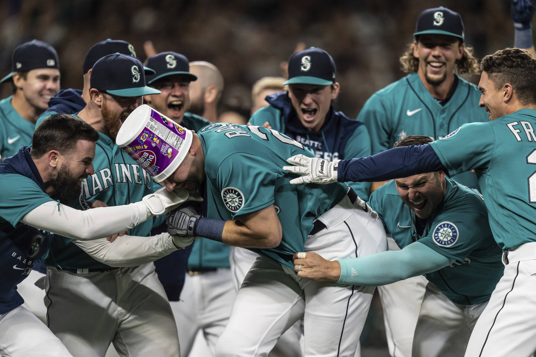 Seattle Mariners including Jesse Winker, left; Ty France, third from right; Logan Gilbert, second from right; and Adam Frazier, right celebrate a home run by Cal Raleigh in ninth inning of a baseball game against the Oakland Athletics, Friday, Sept. 30, 2022, in Seattle. The Mariners won 2-1 to clinch a spot in the playoffs. (AP Photo/Stephen Brashear)