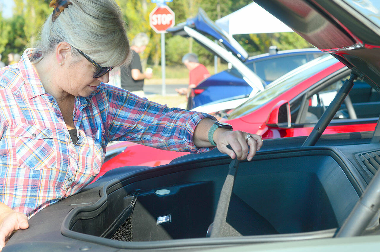 Wendy Davis of Port Townsend takes a look under the hood of her Rivian truck, where an empty storage area is where the engine would have been on a gasoline-powered car. The Rivian’s battery is on the bottom of the truck, much like a skateboard, Davis said. The vehicle can travel 320 miles on a charge, she added. (Diane Urbani de la Paz/For Peninsula Daily News)