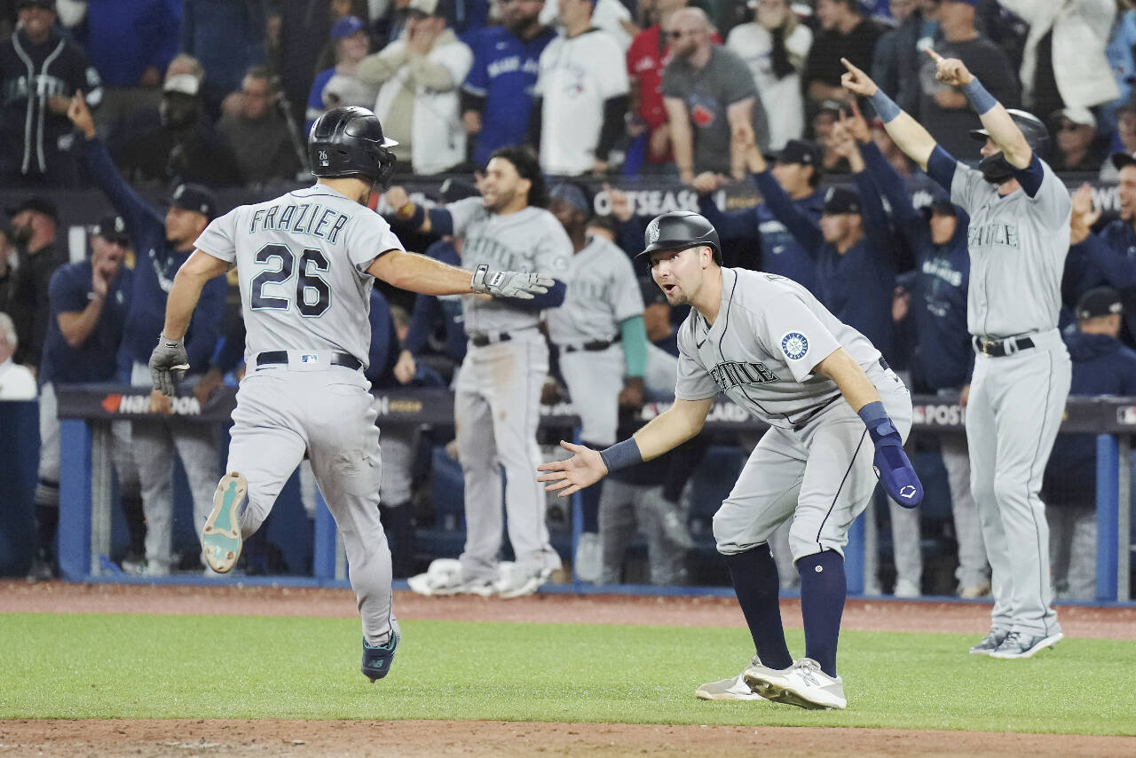 Seattle Mariners' Adam Frazier, left, and Cal Raleigh celebrate after scoring on a three-RBI double off the bat of J.P. Crawford (not shown) against the Toronto Blue Jays during the eighth inning of Game 2 of a baseball AL wild-card playoff series Saturday, Oct. 8, 2022, in Toronto. (Nathan Denette/The Canadian Press via AP)