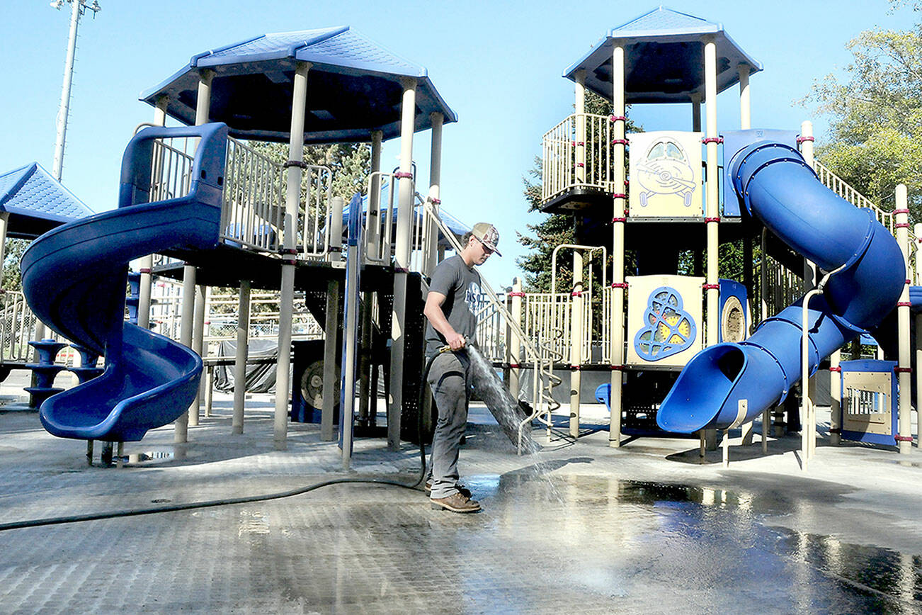 Port Angels Parks & Recreation Department employee Easton Goslin hoses down the concrete underlayment at the playground at Shane Park on the west side of Port Angeles on Wednesday. The playground was closed in mid-September after tiles of rubberized material that made up the play surface began to come loose, creating a hazard to play equipment users. The old tiles have been removed and are awaiting replacement. The playground area remains closed until work can be completed. (Keith Thorpe/Peninsula Daily News)