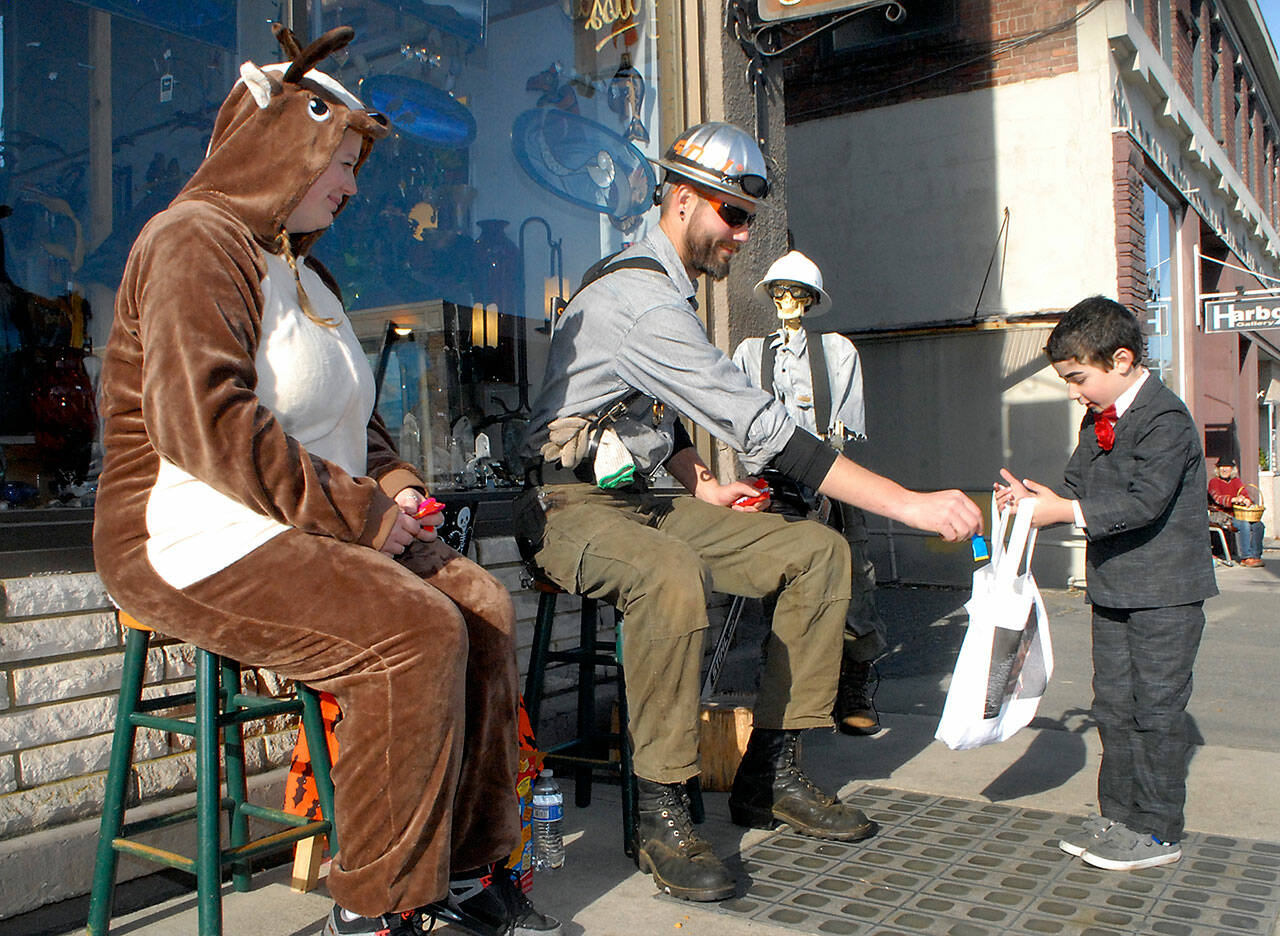 Six-year-old Emmett Stratford of Port Angeles receives a treat from Sarah Ogerly, owner of Olympic Stauned Glass, left, and Mitch Zenobi during Halloween trick or treating in downtown Port Angeles in 2019. (Keith Thorpe/Peninsula Daily News)