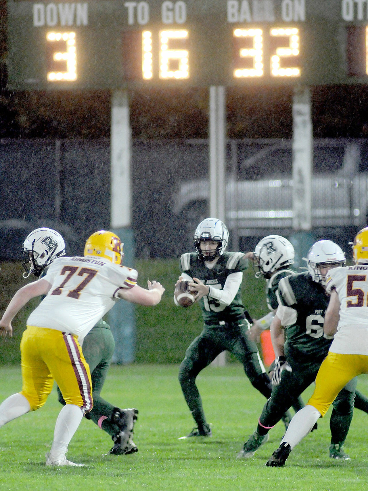 Port Angeles quarterback Parker Nickerson, center, drops back to pass as Kingston’s Tyler Rose tries to break through the line on a rainy Friday evening in Port Angeles. (KEITH THORPE/PENINSULA DAILY NEWS)