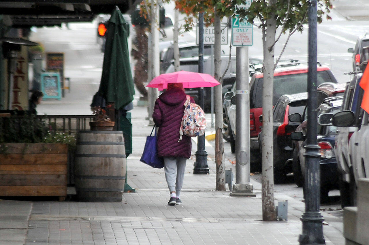 A pedestrian makes their way down West First Street as rain falls upon downtown Port Angeles on Tuesday. A return to seasonal wet weather has prompted county officials to end the annual summer burn ban that had been extended into fall because of exceptionally dry conditions. (Keith Thorpe/Peninsula Daily News)