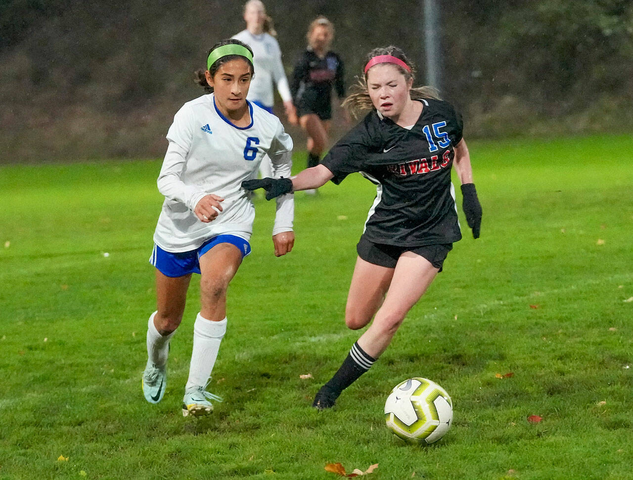East Jefferson’s Ava Shiflett, right, beats out Bellevue Christian’s Lucy Carrel for control during a rain-soaked game on Tuesday at Memorial Field in Port Townsend. (Steve Mullensky/for Peninsula Daily News)