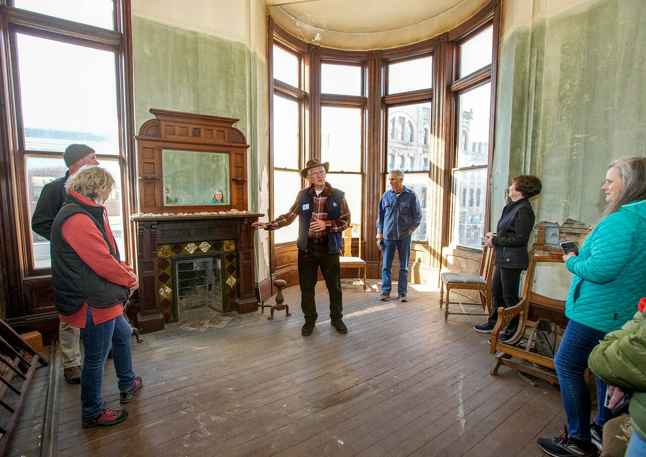 Port Townsend’s Harry Dudley, center, whose family has owned the historic Hastings building in downtown Port Townsend since it was built in 1889, shows off an Italian stone fireplace, one of the highlighted features on the Haunted Histories and Mysteries of Port Townsend tour produced by the Main Street Organization, as he conducts a tour on Friday. (Steve Mullensky/for Peninsula Daily News)