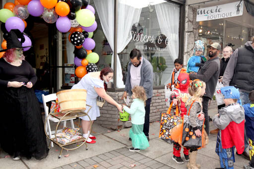 Ariel Juarez, 3, gets a piece of candy from Bre Fitzgerald of Sisters & Co on West First Street in Port Angeles as her dad, Robert Jennings, observes during downtown Halloween festivities on Monday. Nicky Jennings, left, is dressed as the Wicked Witch of the West and Fitzgerald is Dorothy from the Wizard of Oz. (Dave Logan/for Peninsula Daily News)