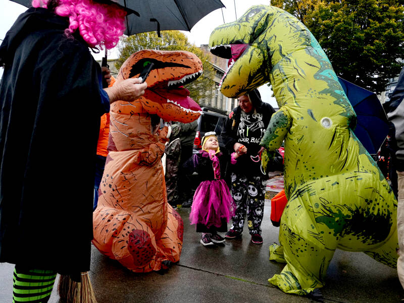 Carmen Walter, 3, looks enamored with the T-Rex while waiting for the start of the annual Halloween Parade in Port Townsend on Monday. (Steve Mullensky/for Peninsula Daily News)