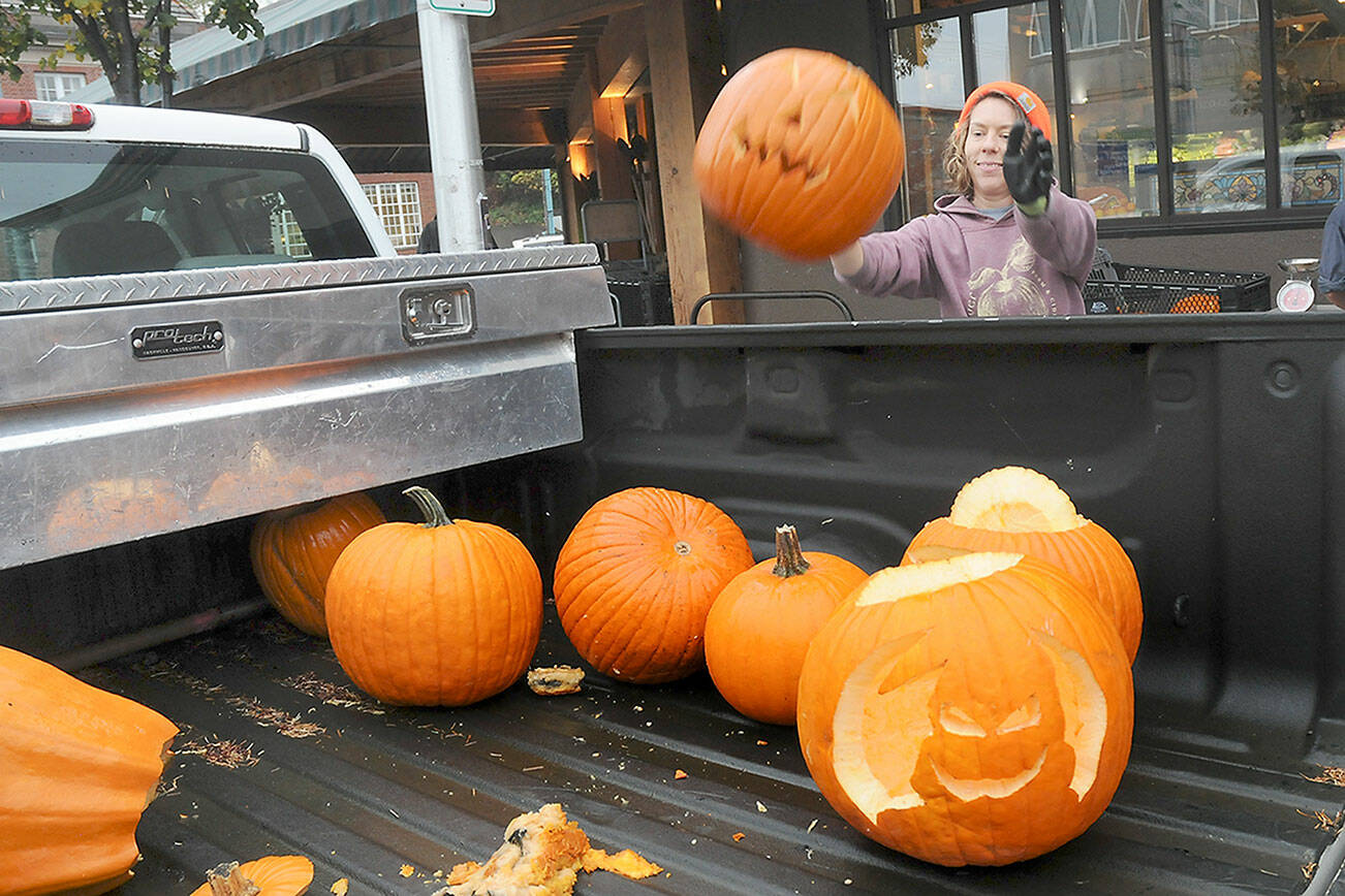 Arlene Jenson, co-founder of Sisterland Farms, tosses a used jack-o-lantern into the back of a truck for recycling during a pumpkin rescue on Friday in front of Country Aire Natural Foods in Port Angeles. The farm, with assistance from the WSU Clallam County Extension, was collecting unwanted pumpkins for composting, keeping them out of landfills and protecting the environment. (Keith Thorpe/Peninsula Daily News)