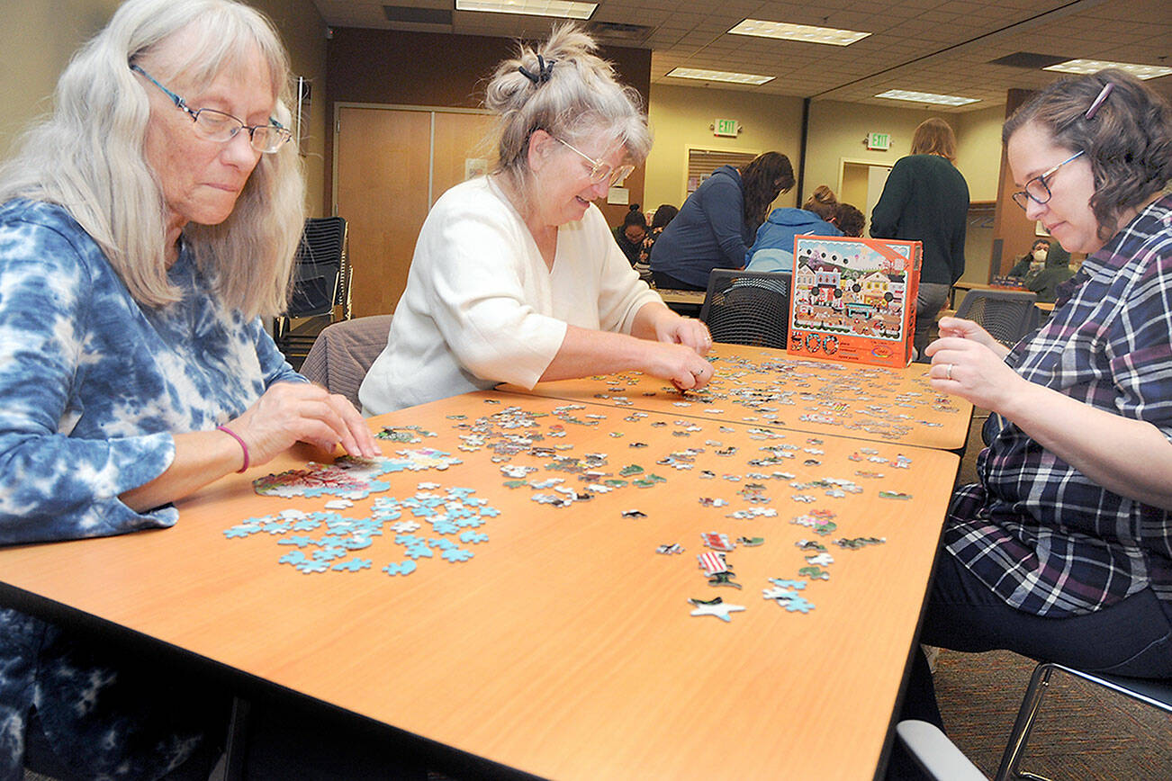 Puzzle solvers, from left, Mary Latson, Kandi Latson and Laura Arndt, all of Port Angeles, attempt to assemble a picture puzzle during a competition on Saturday at the Port Angeles Public Library. The competition pitted about a dozen teams in a timed event to see who could assemble a 500-piece puzzle the quickest, or if the clock expired, which team had the fewest pieces left to place. (Keith Thorpe/Peninsula Daily News)