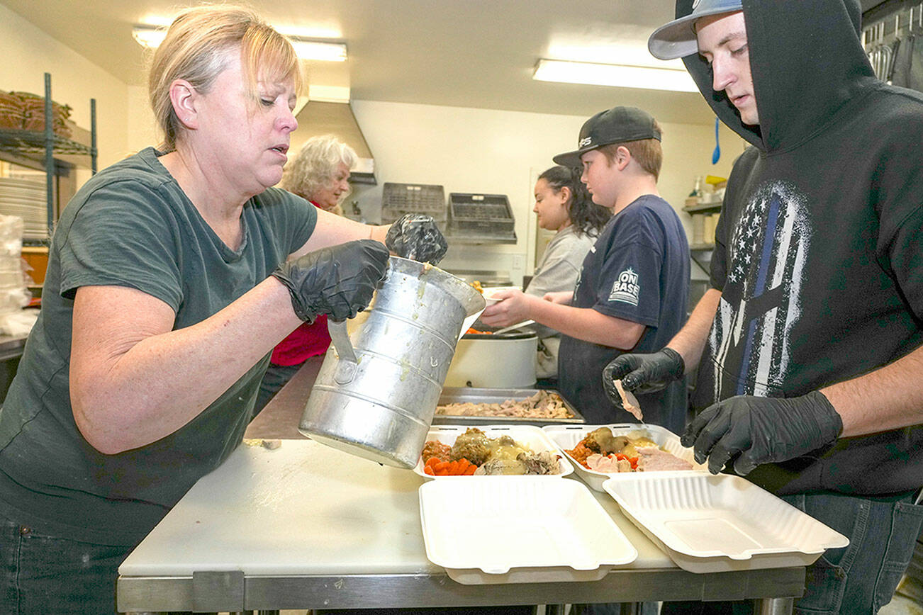 Steve Mullensky/for Peninsula Daily News

Volunteers for the Tri-Area Community Center meals program Gina Landon, ladling gravy while across from her Aiden Glenn arranges turkey slices to complete the assembly line set up to produce over 400 Thanksgiving Day turkey dinners for delivery to homeless camps and senior living facilities in Port Townsend and as far south as Brinnon as well as individual pick-up by those who reserved a dinner. Additional volunteers working in the background on Thursday are Melissa Layer, Rosemary Schmucker and Sean Jones.