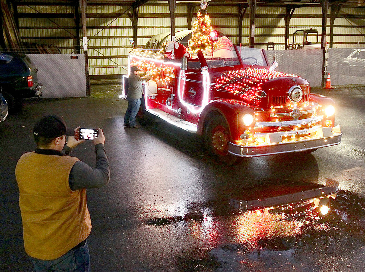 Tyler Gage photographs a fire engine while Adam DeFilippo finishes decorating the old fire engine in preparation for two Operation Candy Cane programs in Port Angeles. (Dave Logan/for Peninsula Daily News)