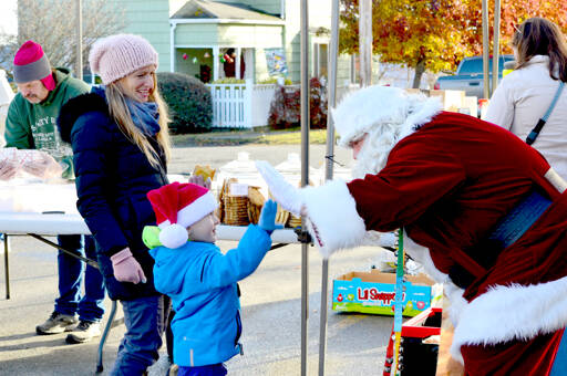 Erin Kluck of Port Townsend watches as her son Kaspar, 4, gives Santa Claus a high five during Saturday’s Uptown Port Townsend Farmers Market. Santa, aka Bryan Hood, said he’ll be manning the Crusty Crumb bakery table again, as the last two farmers markets of the year happen this Saturday and on Dec. 17. (Diane Urbani de la Paz/For Peninsula Daily News)