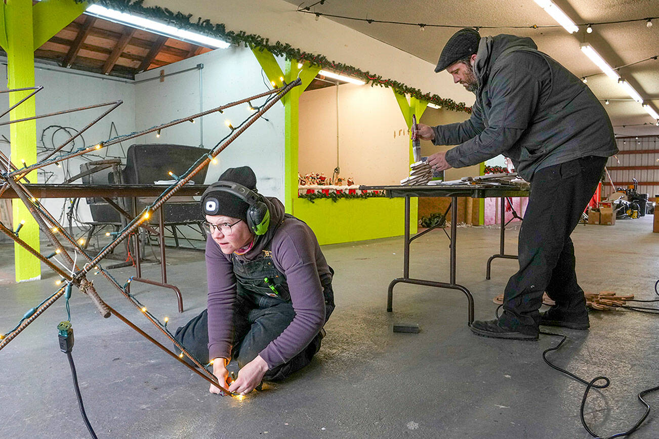 Lilly Gulden checks that the are lights are glowing on a metal Christmas tree skeleton while Jefferson County Fairgrounds manager Danny McEnerney paints lettering for a display all in preparation of the opening of the Magic of Christmas event at the fairgrounds on Thursday. (Steve Mullensky/for Peninsula Daily News)