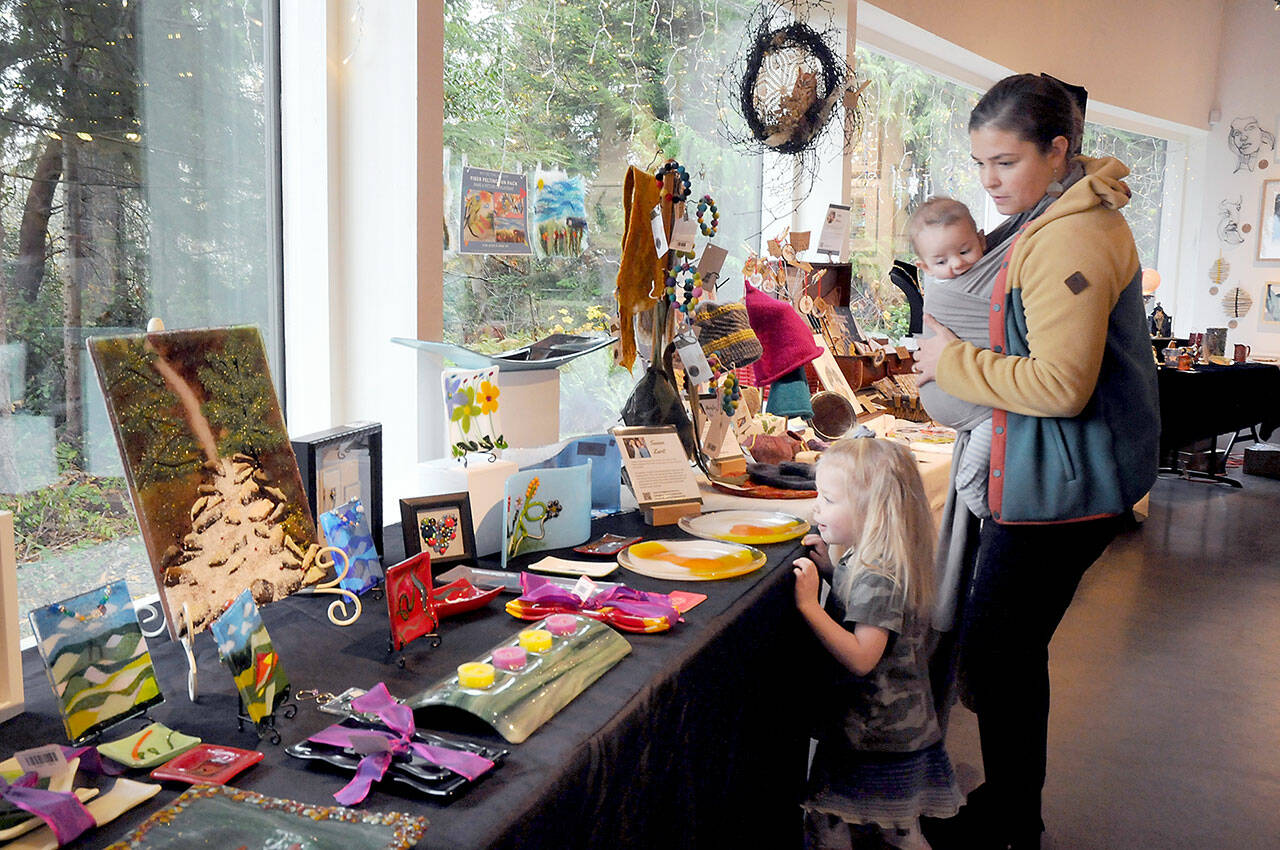 Molly Brown of Port Angeles, and her children, Lucy Brown, 3, and Oliver Brown, 5 months, examine a display of locally-produced art items for sale as gifts on Thursday during the holiday Makers Market at the Port Angeles Fine Arts Center. (Keith Thorpe/Peninsula Daily News)