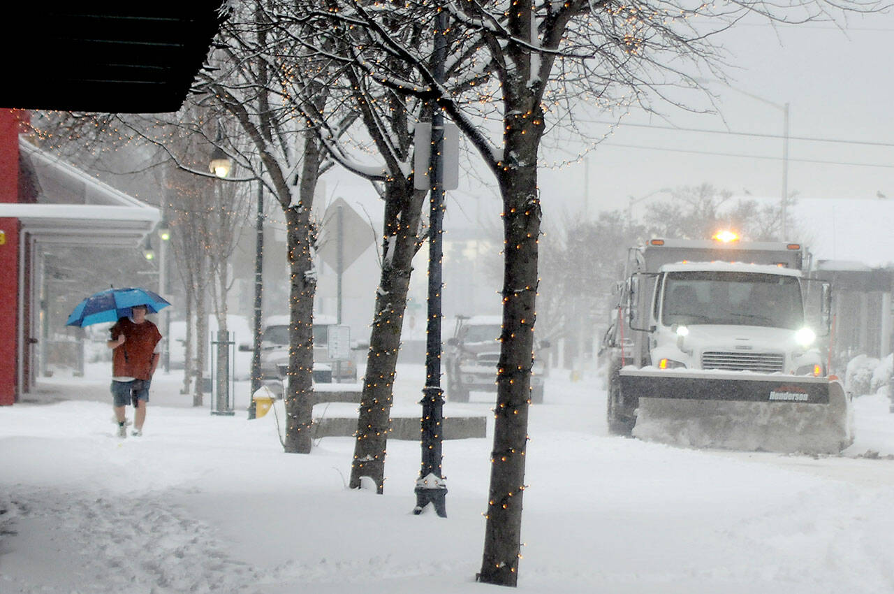 A city snowplow makes its way up West Front Street in downtown Port Angeles on Tuesday as a pedestrian makes his way up a snow-covered sidewalk. (Keith Thorpe/Peninsula Daily News)