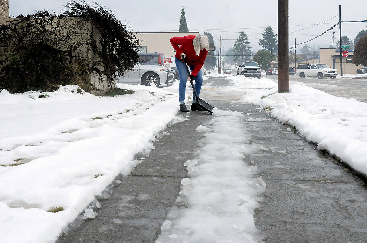 Barb Maynes, a member of First United Methodist Church in Port Angeles, breaks up ice on the sidewalk on the Laurel Street side of the church on Saturday. Warming temperatures and rain were helping to melt nearly a foot of snow that had fallen earlier in the week, but remaining accumulated ice required physical attention in many locations. (Keith Thorpe/Peninsula Daily News)