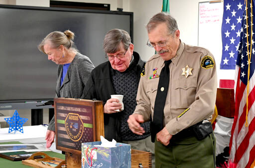 Outgoing Clallam County Sheriff Bill Benedict, right, looks at a variety of gifts and tributes at a retirement party on Tuesday in Port Angeles. Pictured with Benedict is wife, Kathy, and longtime friend Jack Flanagan. (Michael Dashiell/Olympic Peninsula News Group)