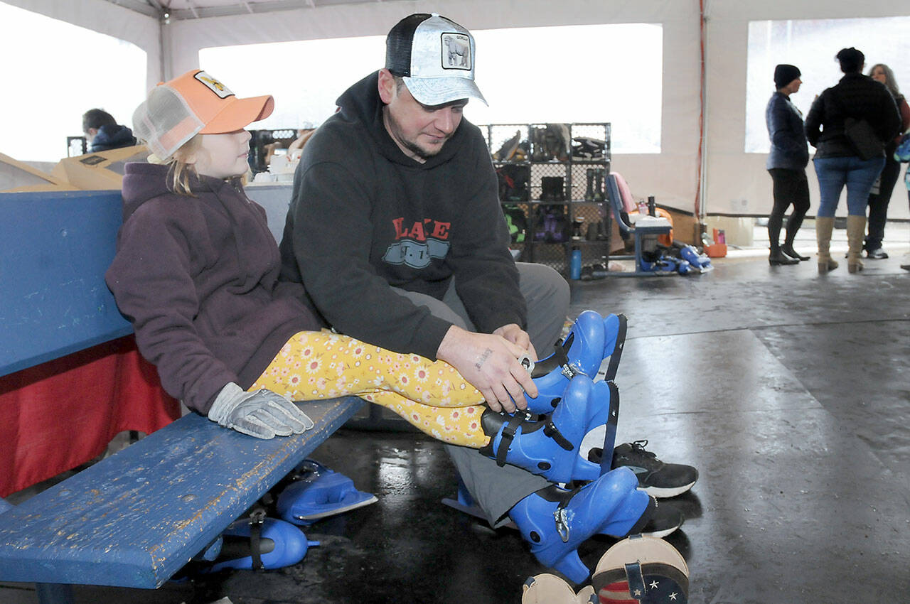 Steve Evans of Port Angeles assists his daughter, Ruby Evans, 7, with her skates prior to a session on the ice on Friday at the Port Angeles Winter Ice Village. (KEITH THORPE/PENINSULA DAILY NEWS)