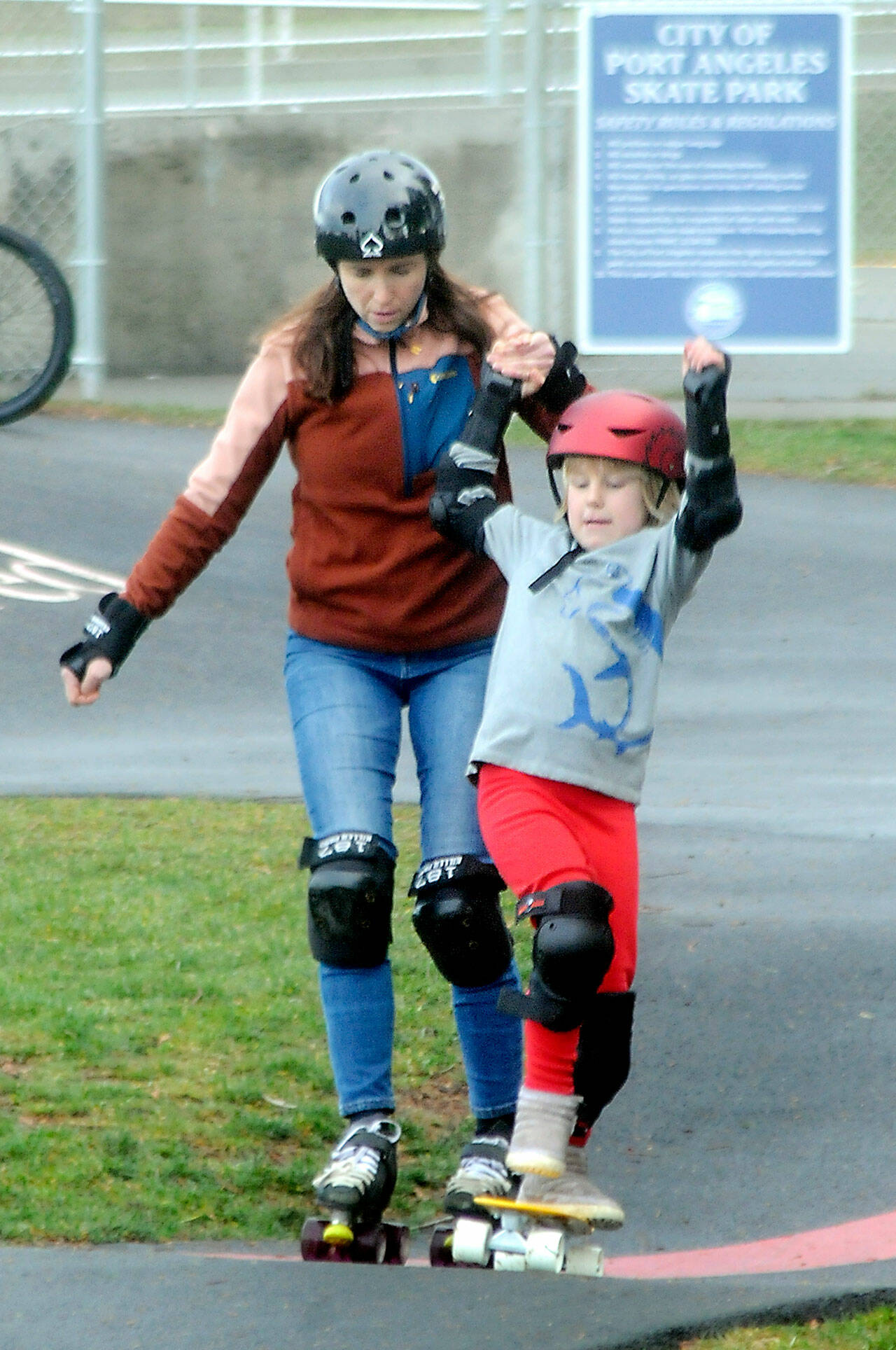 Shawna Bebo of Sequim lends a balancing hand to her son, Enzo Bebo, 7, at the Port Angeles Pump Track at Erickson Playfield in Port Angeles last weekend. The pair were on a family outing with a stop at the popular attraction. The 14,442-square-foot pump track is the largest Velosolutions pump track in the Pacific Northwest and the first public adaptive track in the nation. (Keith Thorpe/Peninsula Daily News)