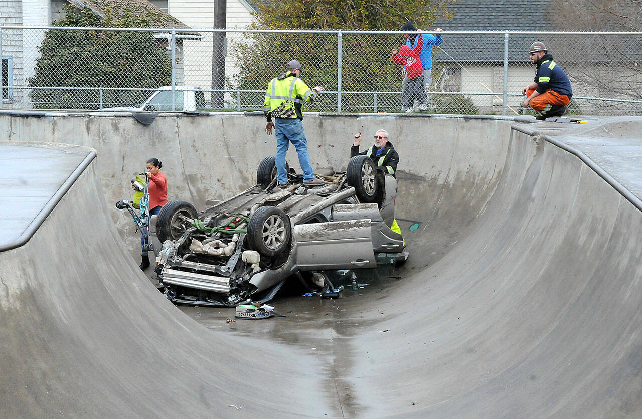 Towing personnel work out a strategy to remove an overturned car from the Port Angeles Skate Park at Erickson Playfield on Wednesday after the car crashed into the park on Tuesday night. (Keith Thorpe/Peninsula Daily News)