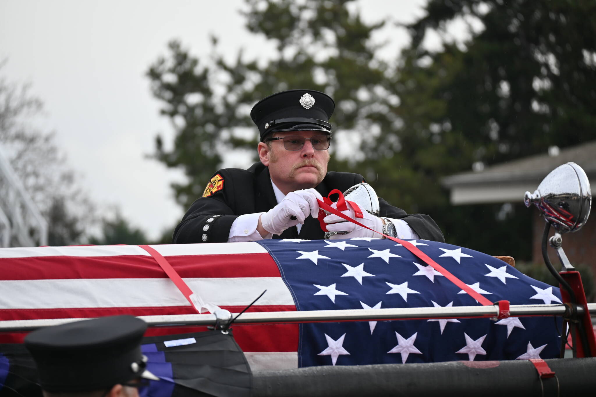 Scott Dickson, longtime firefighting partner of Capt. Charles Chad Cate, removes straps securing Cate’s casket at a memorial Saturday afternoon for the firefighter who was found deceased while on shift on Jan. 12. (Olympic Peninsula News Group)