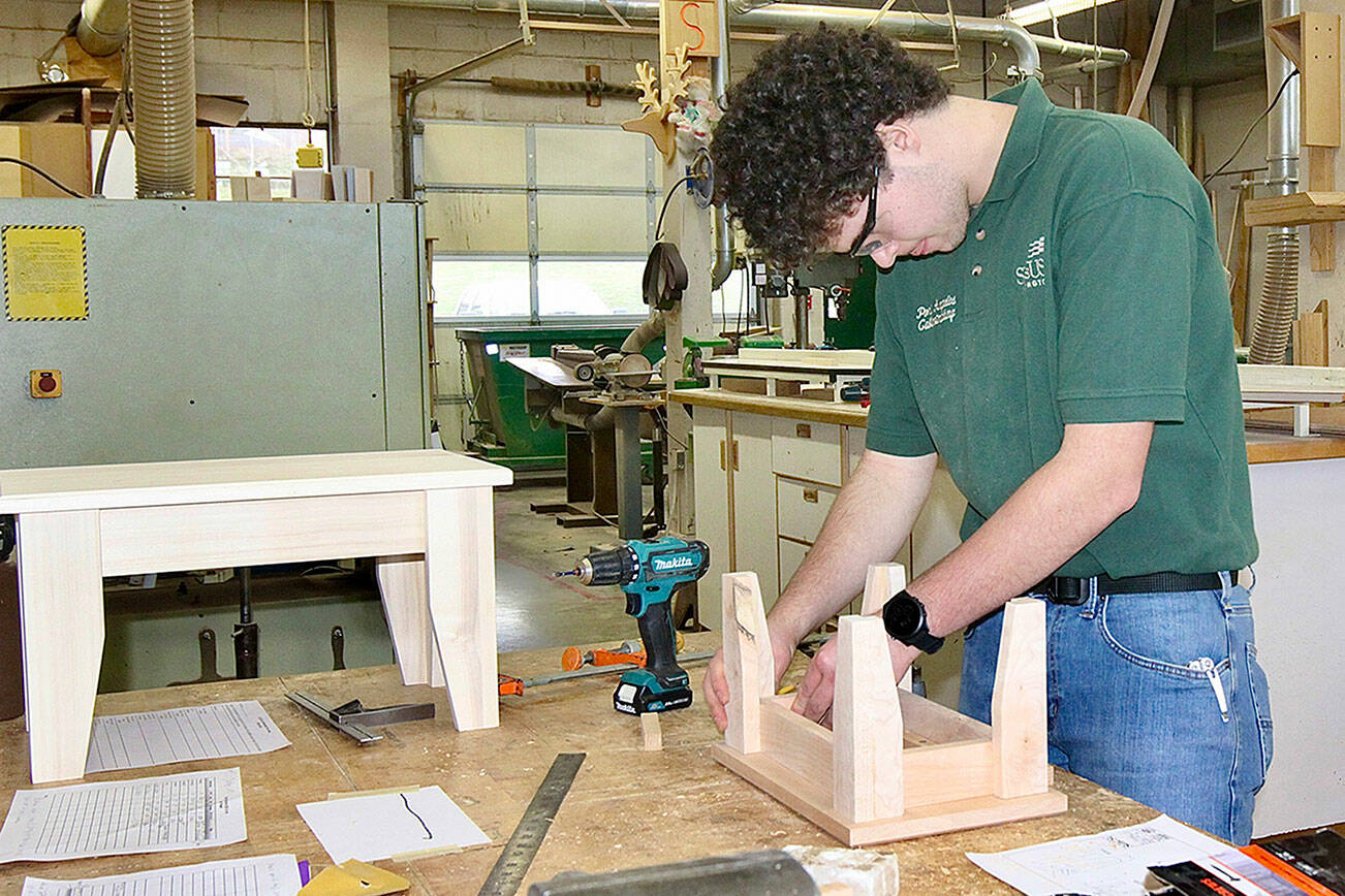 Brock Tejeda, a high school senior, fits together his carefully crafted pieces of wood to make a step stool just like the larger finished sample on the left. Port Angeles High School hosted a Skills USA Olympic Regional contest in the woodshop at the school on Saturday. The contest involved students making in eight hours from precise directions a small step stool using their skills and the shop’s many tools and machines. Joe Shideler is the woodshop teacher, but retired woodshop teacher Tim Branham was the enabler who brought the contest back to the school after a four-year COVID absence. There were five high school contestants including one girl. Skills USA sponsors over 50 skills across the country. PAHS participated in the carpentry and precision machinery areas. (Dave Logan/for Peninsula Daily News)