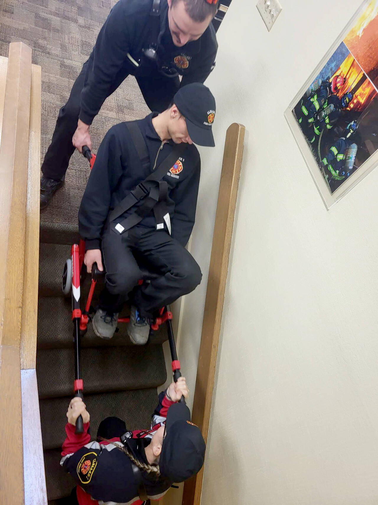 Captain/EMT Tyler Gear, at top, and Firefighter/Paramedic Margie Brueckner, bottom, train on Clallam 2’s new stair chair by lowering Recruit Theo Saxe down a flight of stairs.