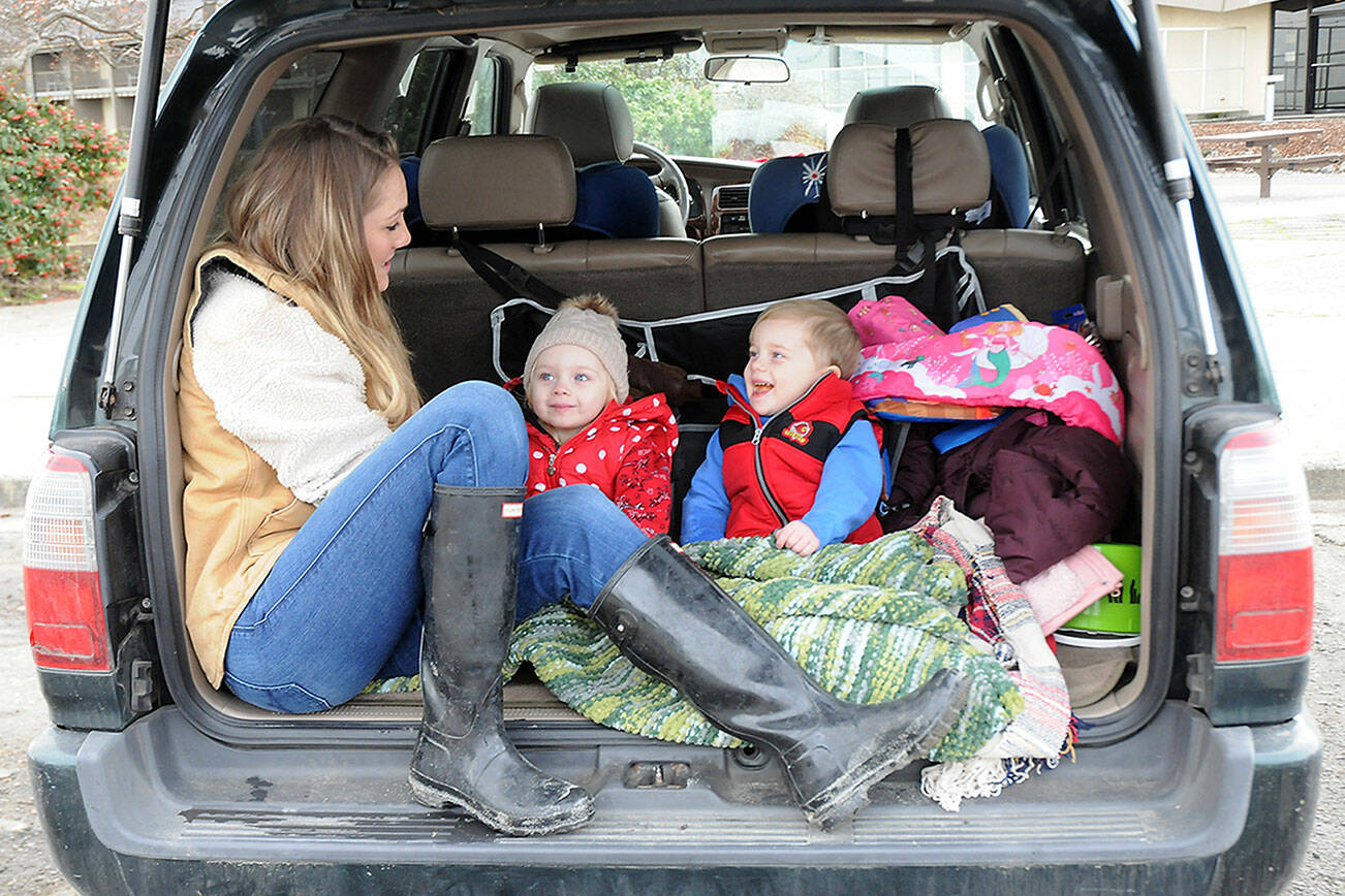Katie Roszatycki of Port Angeles and her children, June Roszatycki, 2, and Asher Roszatycki, 3, sit in the back of their car waiting for the delivery of dry shoes and socks from another family member after an outing to Hollywood Beach on Thursday. The family was keeping themselves entertained in the parking lot at Port Angeles City Pier. (Keith Thorpe/Peninsula Daily News)